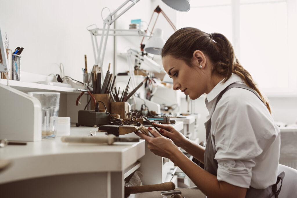 Focused on a process. Portrait of young female jeweler focused on creating a silver ring at her