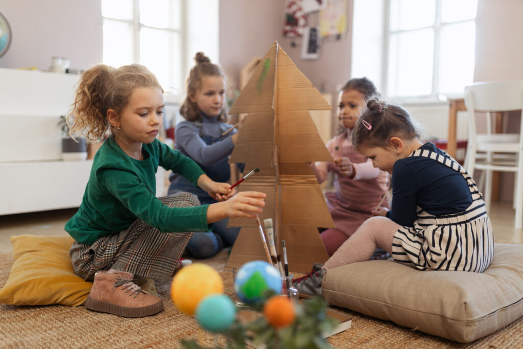 Group of little girls painting cardboard tree at creative art and craft class at school