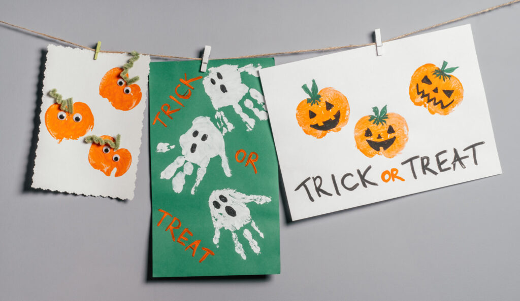 Three Halloween childrens pumpkin apple prints and ghosts handprints drawings hanging on rope on