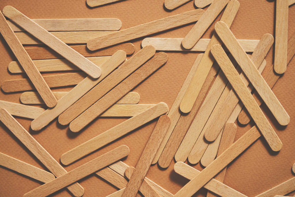 Wooden popsicle sticks, scattered on top of a beige background